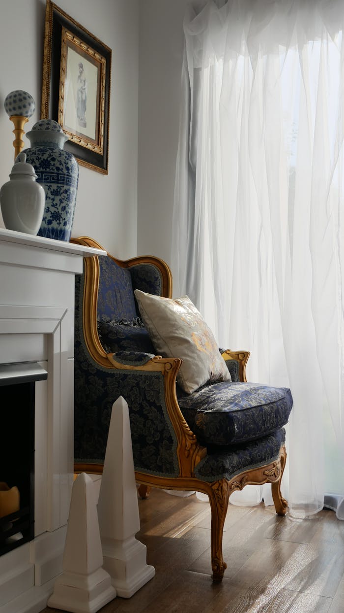 A stylish room interior featuring a classic armchair, vases, and curtains by a bright window.