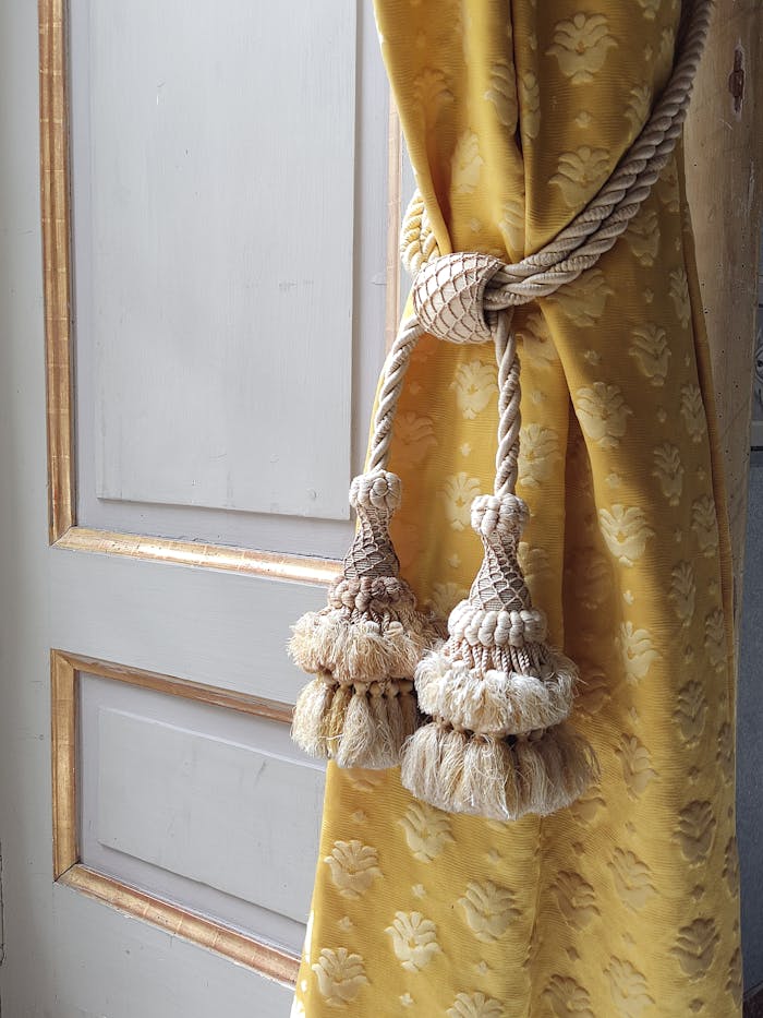 Close-up view of a luxurious yellow curtain with decorative tassel tieback against a door.